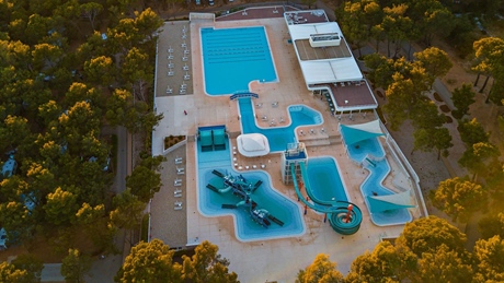 Aerial view of a large outdoor swimming pool with slides and surrounding trees