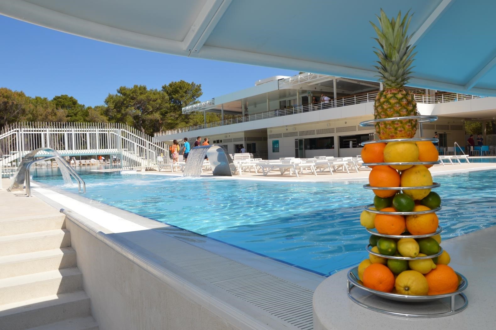 A swimming pool with a fruit display and a modern building in the background